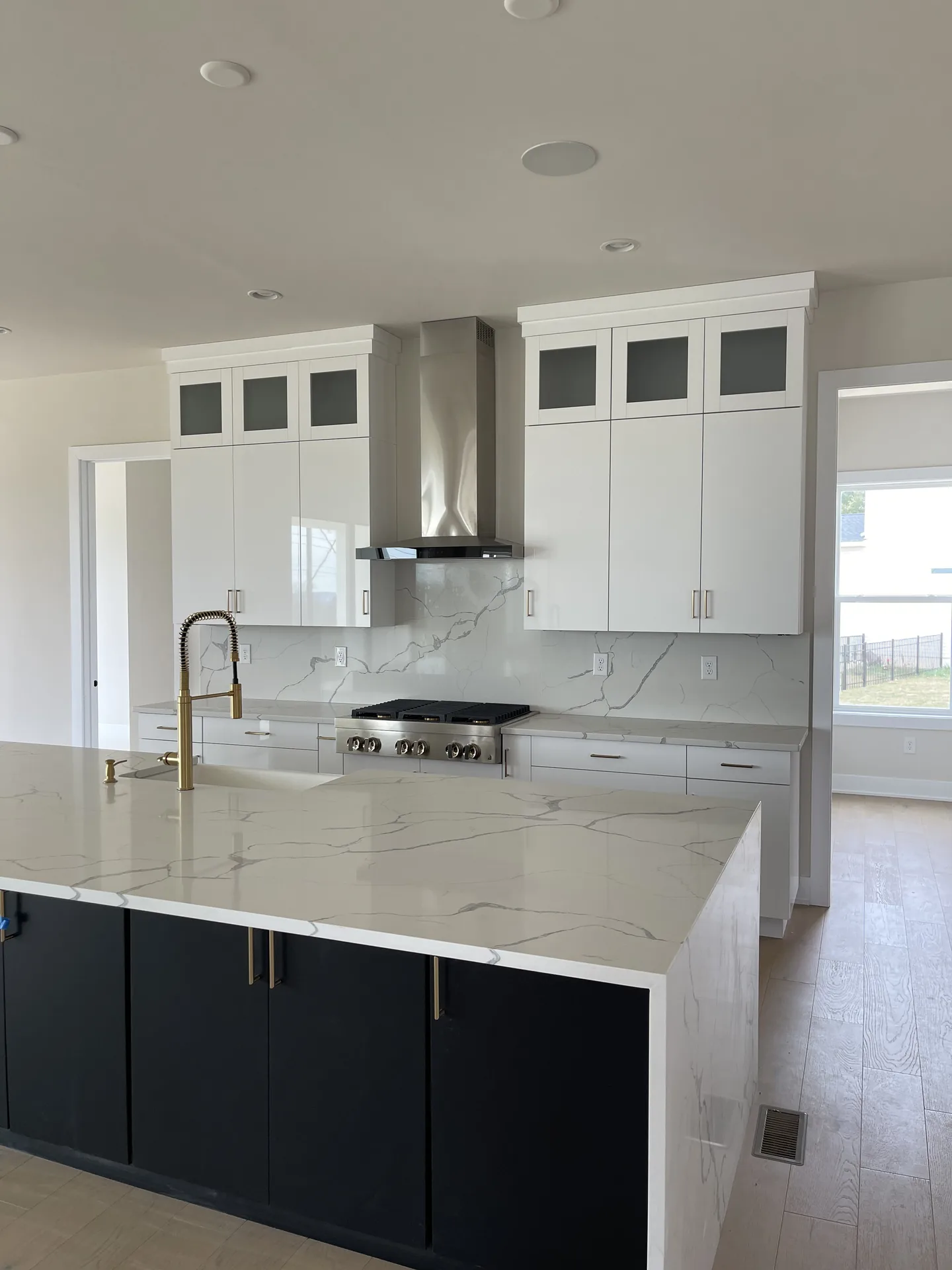 Luxury kitchen with calacatta marble waterfall island, navy base cabinetry, brass faucet, and stainless pro-style range