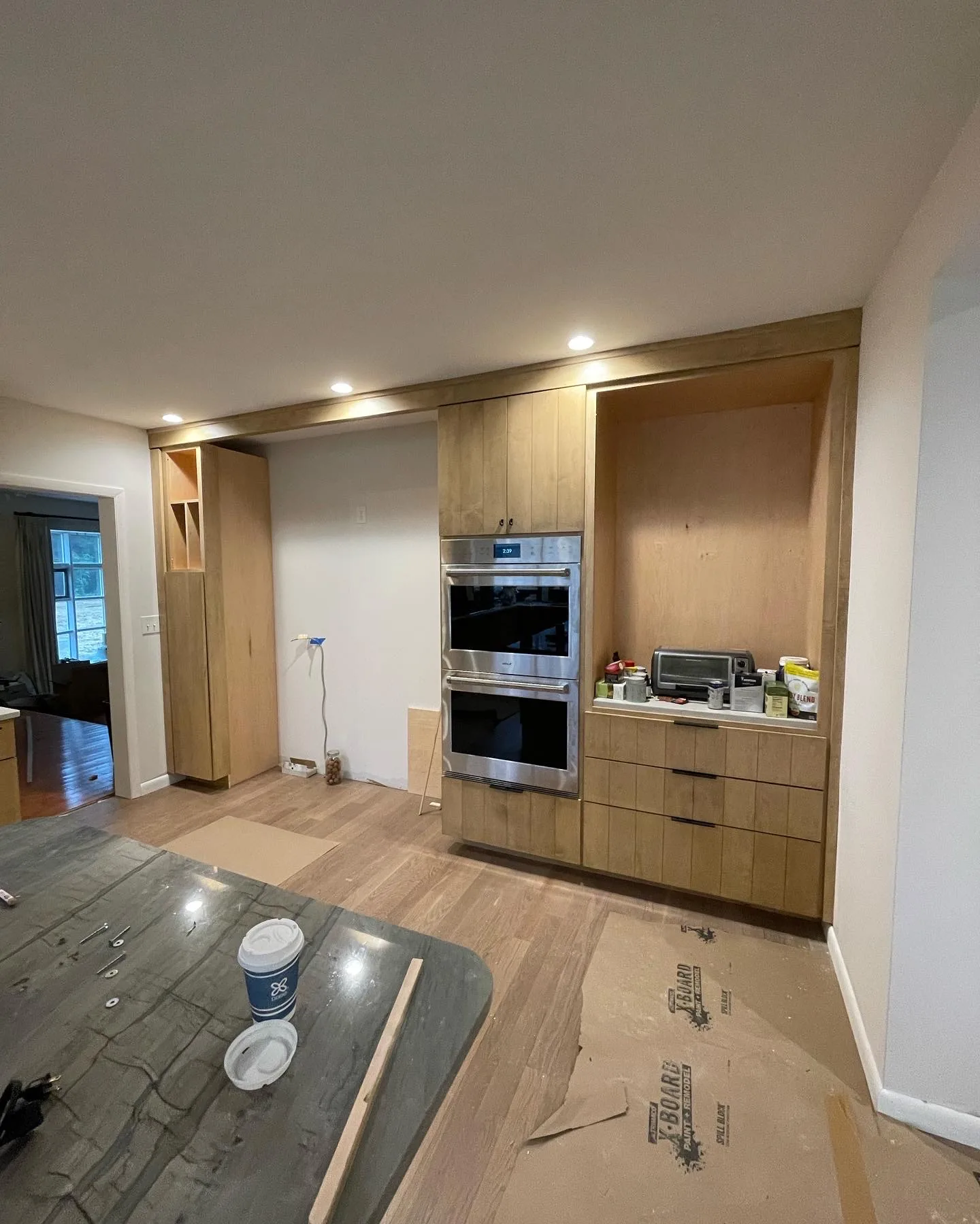 Natural wood kitchen cabinetry with stacked double ovens and a matching wood island under installation